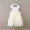 A white toddler girl's party dress with a lace bodice and layered tulle skirt, hanging on a white plastic hanger against a neutral gray background.