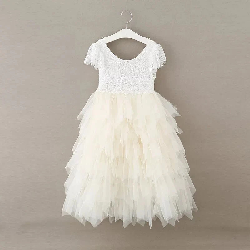 A white toddler girl's party dress with a lace bodice and layered tulle skirt, hanging on a white plastic hanger against a neutral gray background.